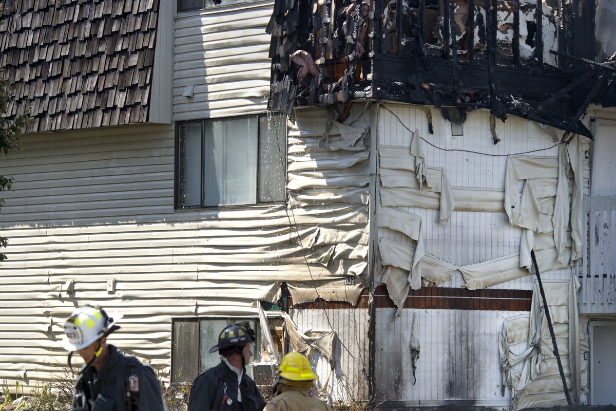 Fire officials view the extensive damage to a three-story apartment building at the corner of Augusta and Astor, July 2, 2015, in Spokane, Wash. The fire swept through the top floor and burned the roof off. (Dan Pelle / The Spokesman-Review)