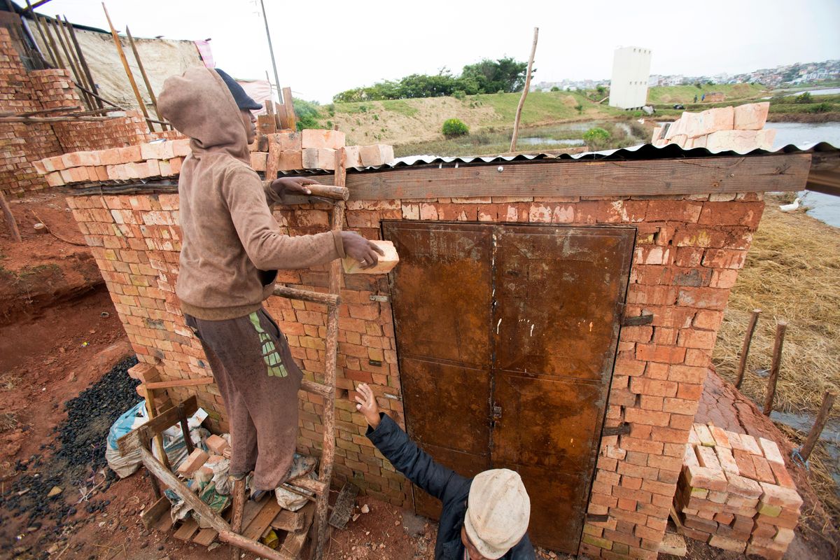 A man weighs down the roof of his home with bricks to stop it from flying away during bad weather in Antananarivo, Madagascar, Saturday, Feb. 5, 2022. Weather officials forecast that the full force of Cyclone Batsirai is to hit Madagascar Saturday evening. (Alexander Joe)