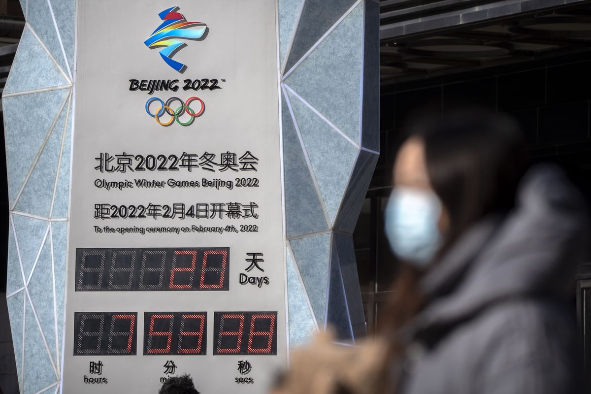 A woman wearing a face mask to protect against COVID-19 walks past a clock counting down the time until the opening ceremony of the 2022 Winter Olympics in Beijing, Saturday, Jan. 15, 2022. As the Beijing Winter Olympics loom, the Chinese capital is stepping measures to keep the coronavirus at bay including suspending most access to Tianjin, an adjacent major city which is dealing with an outbreak of the highly contagious omicron variant. These outbreaks are posing a test to its "zero-tolerance" COVID-19 policy and its ability to successfully host the Winter Olympics. (Mark Schiefelbein)