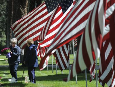 Kathleen Danly, 63, left, and her sister Maxine Smith, 84, lay mums on the grave of their parents, Ernest and Gertrude Clem, on Wednesday at Fairmount Memorial Park in Spokane. Fairmount sets out more than 2,200 American flags every year for Memorial Day.  (Dan Pelle / The Spokesman-Review)