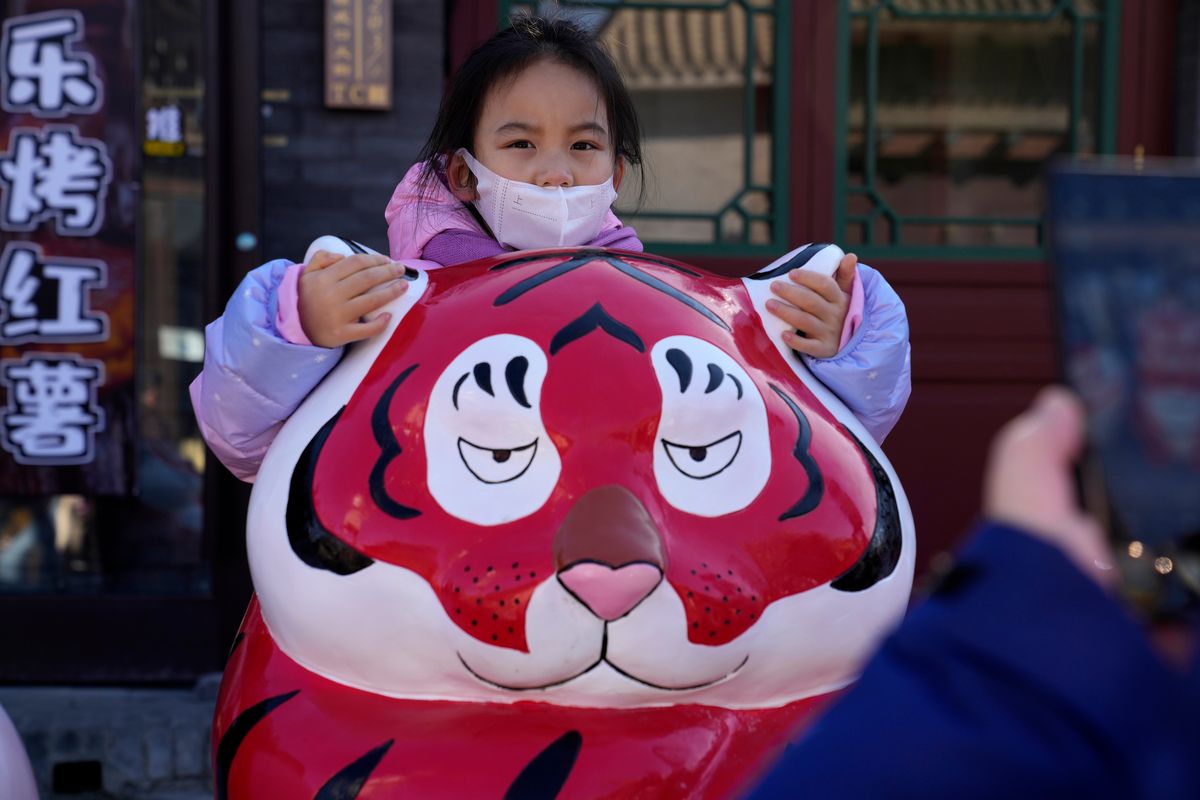 A child wearing a mask holds on to the ears of a Tiger sculpture on the first day of the Lunar Year of the Tiger in Beijing, China, Tuesday, Feb. 1, 2022. (Ng Han Guan)