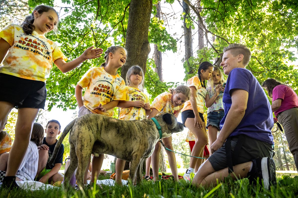 At Camp Sparkle, Maverick, and his owner Hayley Jewell with the Ruff Revue dog performance group, greets kids attending Camp Sparkle, left to right, Nellie Bower, 9, Scarlett Bozo, 7, Amelia Kuhn, 7, and Bella Kuhn, 11, on Tuesday in Manito Park. The Cancer Pathways day camp had 21 kids and teens impacted by cancer, either their own diagnosis or a diagnosis of a family member, offering a chance to have some summer fun.  (COLIN MULVANY/THE SPOKESMAN-REVIEW)