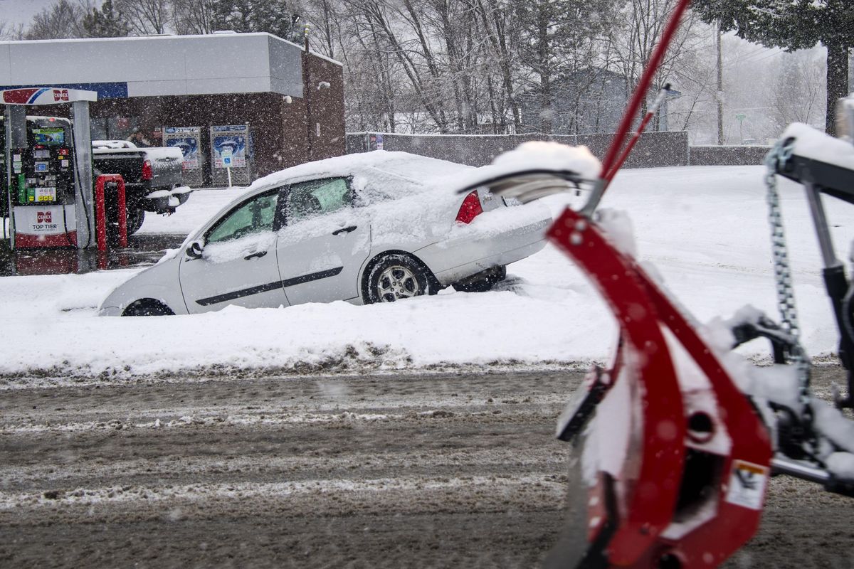 A snowplow passes a Ford Focus that slid off the road at the corner of Euclid and Market during Friday’s snowstorm, Dec. 15, 2017, in Spokane, Wash. (Dan Pelle / The Spokesman-Review)