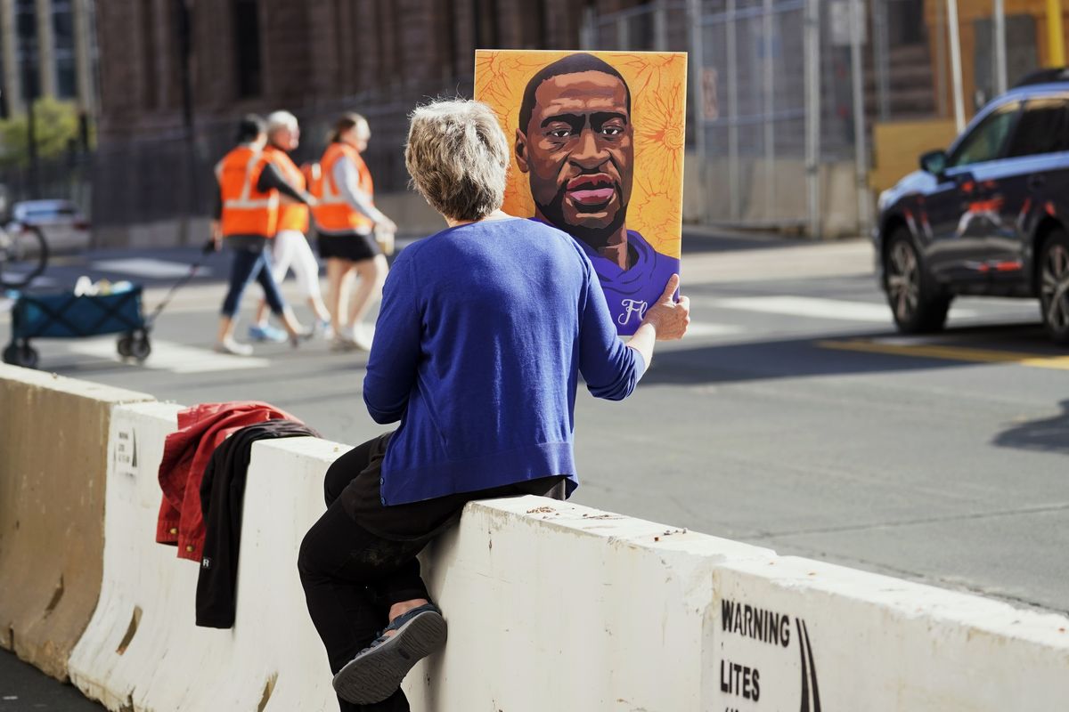 A woman holds a George Floyd picture while seated on a concrete barrier near the Hennepin County Government Center Monday, April 5, 2021, in Minneapolis where the second week of testimony in the trial of former Minneapolis police officer Derek Chauvin continues. Chauvin is charged with murder in the death of George Floyd during an arrest last May in Minneapolis.  (Jim Mone)