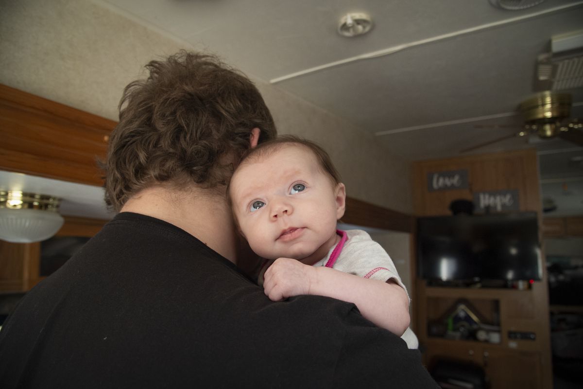 Two-month-old Clara Jean Hoover clings to her father Jason Hoover who is trying to burp her inside the fifth-wheel trailer belonging to Hoover and fiancee Sage Butler, who are staying in the KOA campground in Spokane Valley since their family home in Malden burned down on Labor Day 2020, when Sage was 8 months pregnant. The couple lost many things of sentimental value, besides the home Sage’s grandfather left to her mother. The trailer was purchased with money from a GoFundMe account and the generosity of donors has supplied them with diapers and baby wipes, but the couple is still trying to find hope for the future.  (Jesse Tinsley/THE SPOKESMAN-REVIEW)