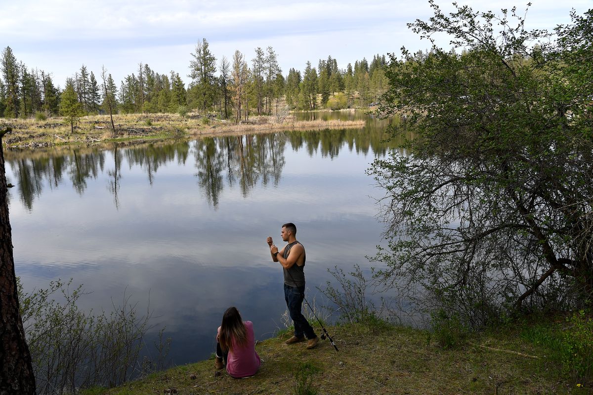 J.P. Dutton baits a hook as Kayla Rambo looks on after they hiked on DNR land to access Chapman Lake for an afternoon of fishing on May 5, 2021, outside Cheney.  (TYLER TJOMSLAND/The Spokesman-Review)
