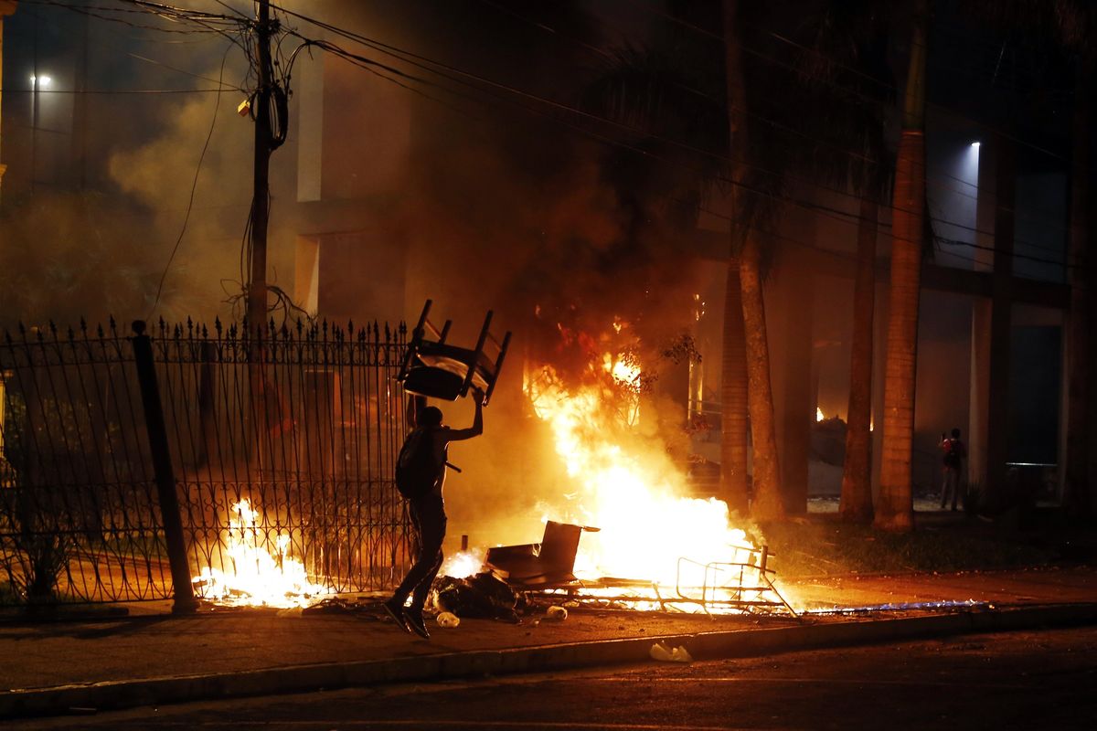 A protester carries a chair to a fire outside the congress building during clashes between police and protesters opposing an approved proposed constitutional amendment that would allow the election of a president to a second term, in Asuncion, Paraguay, Friday. Some protesters broke through police lines and entered the first floor, where they set fire to papers and furniture. Police used water cannon and fired rubber bullets to drive demonstrators away from the building while firefighters extinguished blazes inside. (Jorge Saenz / Associated Press)