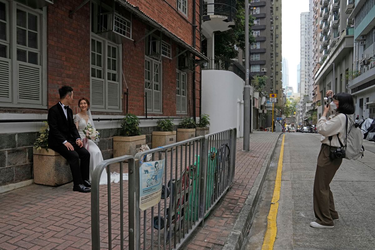 A photographer wearing a face mask takes a wedding photograph of a couple on a street in Hong Kong, Sunday, March 13, 2022. The territory