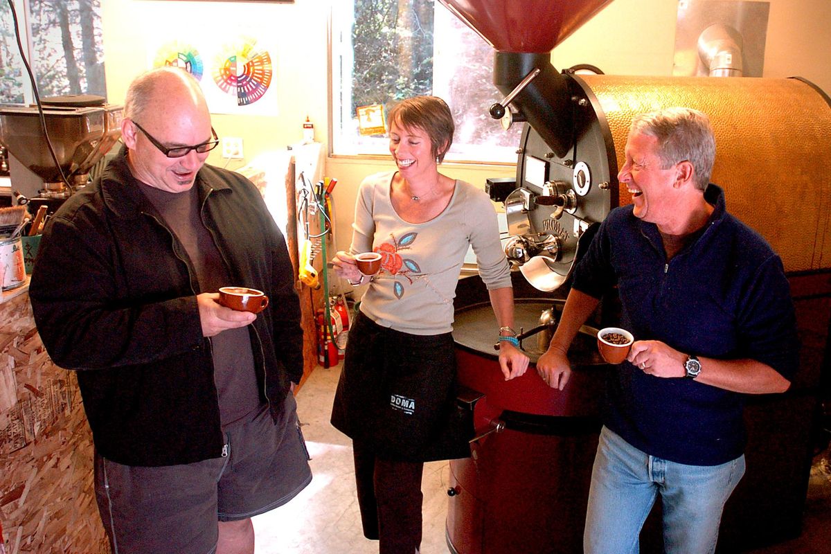 Terry Patano, left, Rebecca Patano, center, and Paul Moynihan stand around their small batch roaster at their home in rural Post Falls. Doma will give away free coffee drinks all day Friday at their coffee bar on Seltice Way. This includes drip coffee, pour-overs and all espresso-based drinks. (Jesse Tinsley / The Spokesman-Review)