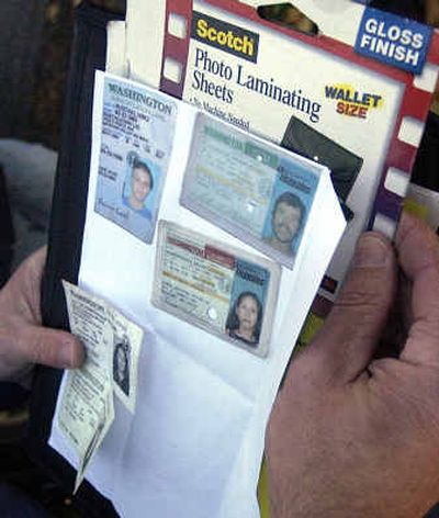 
WSP Trooper Jim Hays holds up various Washington State driver's licenses that officers found in the home they raided on Coleman Road in the Spokane Valley Wednesday. The photo laminating sheets can be used to make fake IDs. 
 (Liz Kishimoto / The Spokesman-Review)