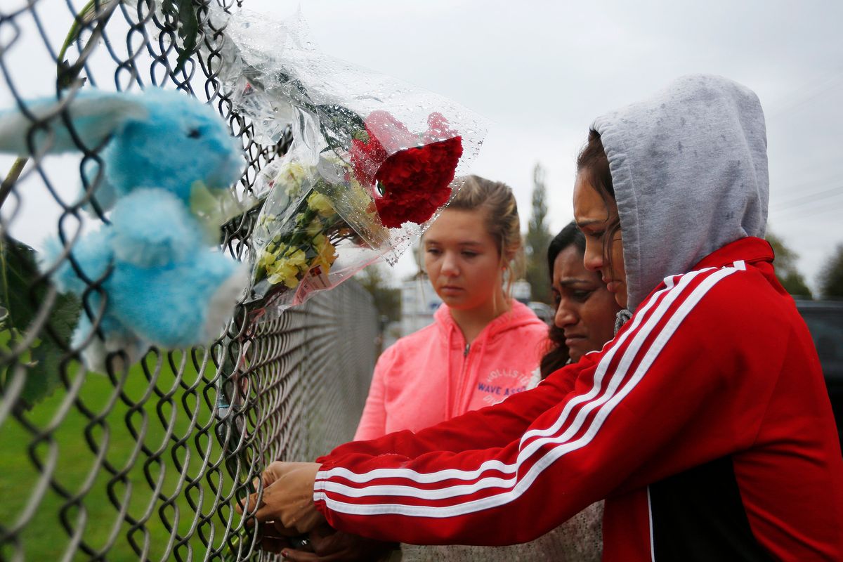 Student Tyanna Davis, right, her mother, center, and another student place flowers Saturday at the high school fence. (Associated Press)