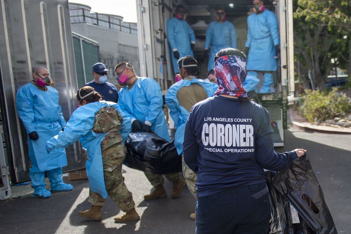 In this Tuesday, Jan. 12, 2021 photo provided by the LA County Dept. of Medical Examiner-Coroner, Elizabeth "Liz" Napoles, right, works alongside the National Guard who are helping to process COVID-19 deaths that are be placed into temporary storage at LA County Medical Examiner-Coroner Office in Los Angeles. Just a little more than a year after California announced its first case of coronavirus, the nation