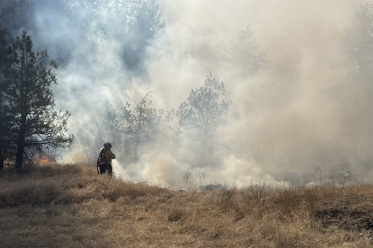 A firefighter is working to extinguish flames Friday afternoon west of downtown Spokane. (Garrett Cabeza/S-R)