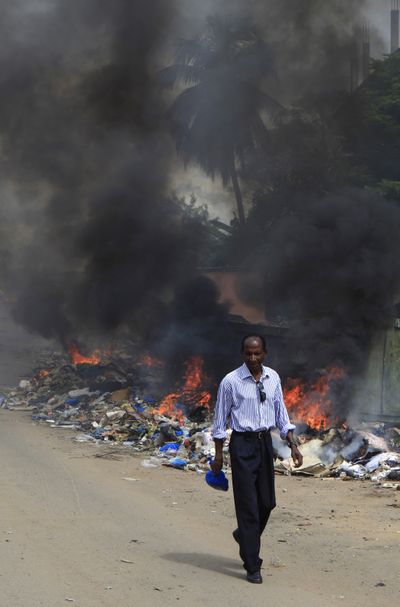 A man walks past burning trash and bodies in the Adjame neighborhood of Abidjan, Ivory Coast, on Saturday. (Associated Press)