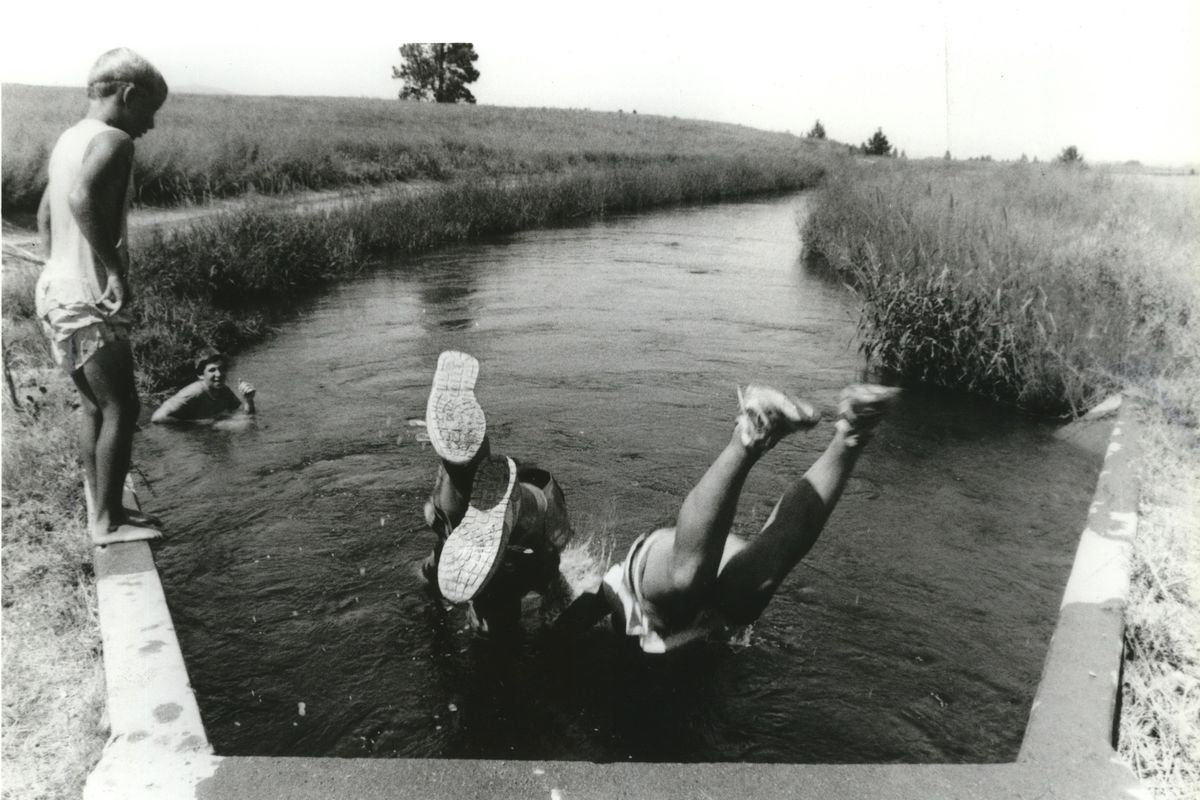 Shane Hubbard, left, and Jason Noble, second from left, watch Erade Smith and Dale Viall, all of Post Falls, cool off in an irrigation canal in Post Falls near Huetter Road in 1990. The water is diverted from the Spokane River towards the Rathdrum Prairie for local grass growers, part of a network of irrigation ditches started by various land developers before the turn of the 20th century.  (Jesse Tinsley/The Spokesman-Review)