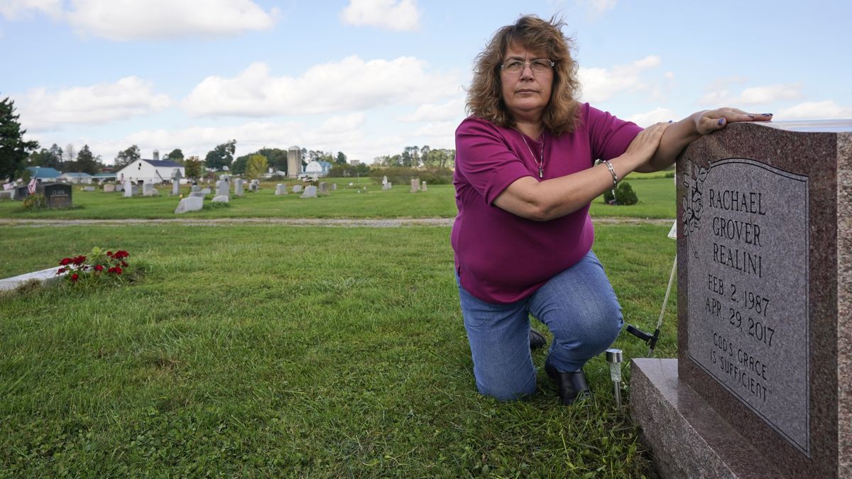 Sharon Grover rests her hands on the gravestone for her daughter, Rachael, Tuesday, Sept. 28, 2021, at Fairview Cemetery in Mesopotamia, Ohio. Grover believes her daughter started using prescription painkillers around 2013 but missed any signs of her addiction as her daughter, the oldest of five children, remained distanced.  (Tony Dejak)
