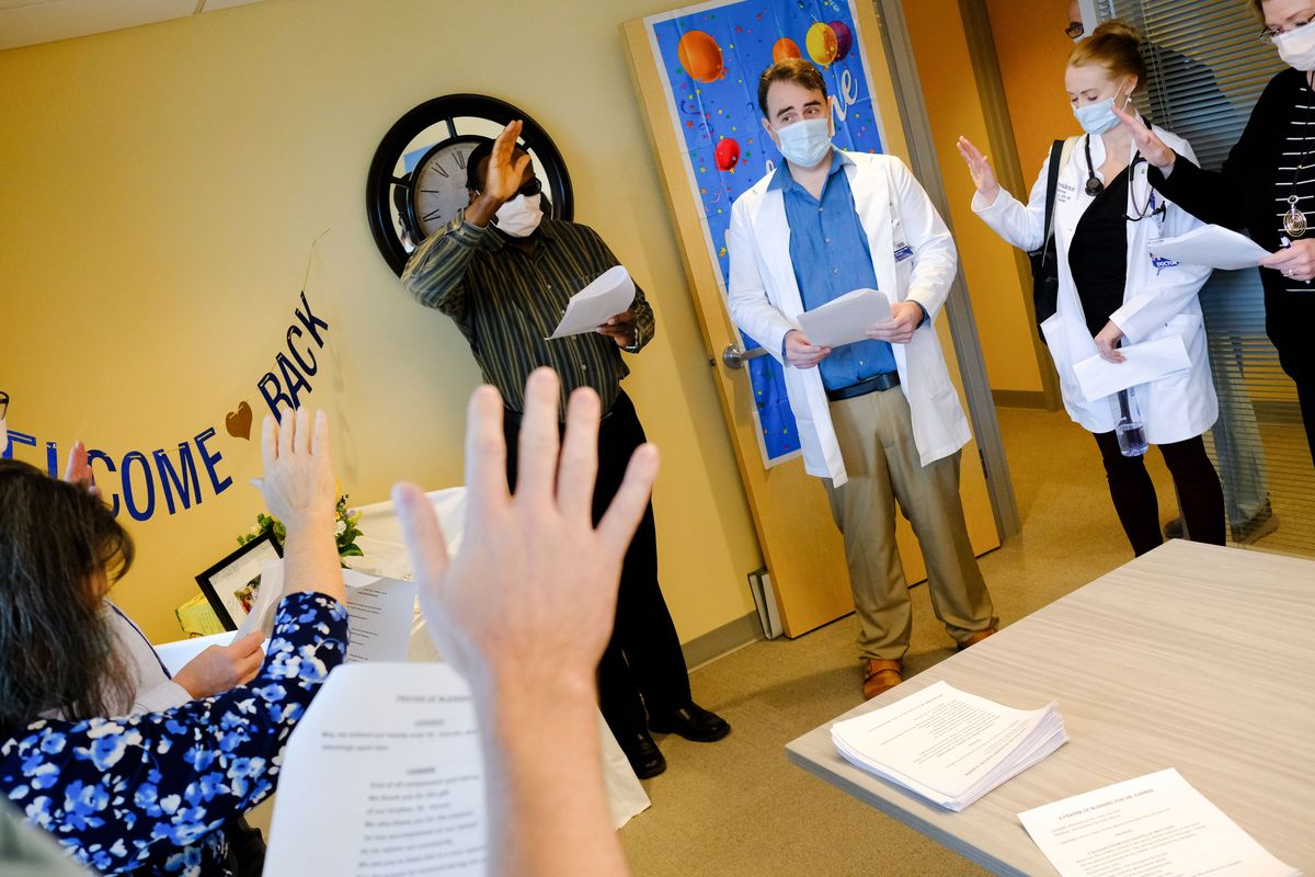 Staff members at Providence Holy Family Hospital raise their hands Tuesday as they offer a blessing for Dr. Kyle Varner, center, after his return from helping refugees on the Ukraine–Poland border who were fleeing the Russian invasion.  (Tyler Tjomsland/The Spokesman-Review)