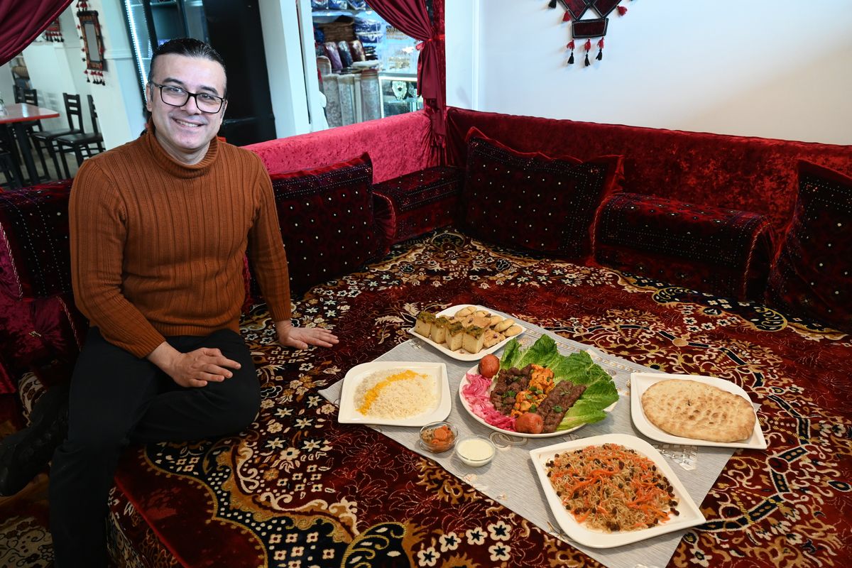 Restauranteur Nasrollah Mohammadi sits in a booth in the Emran Restaurant at 1817 N. Division St. in Spokane on Jan. 25, 2024, beside a full spread of dishes often served family style in these booths where customers can eat sitting on rugs and pillows in a traditional Afghani way. Mohammadi and his family have western style seating as well as a retail store and display area for traditional Afghan clothing, crafts and food.  (Jesse Tinsley/The Spokesman-Review)
