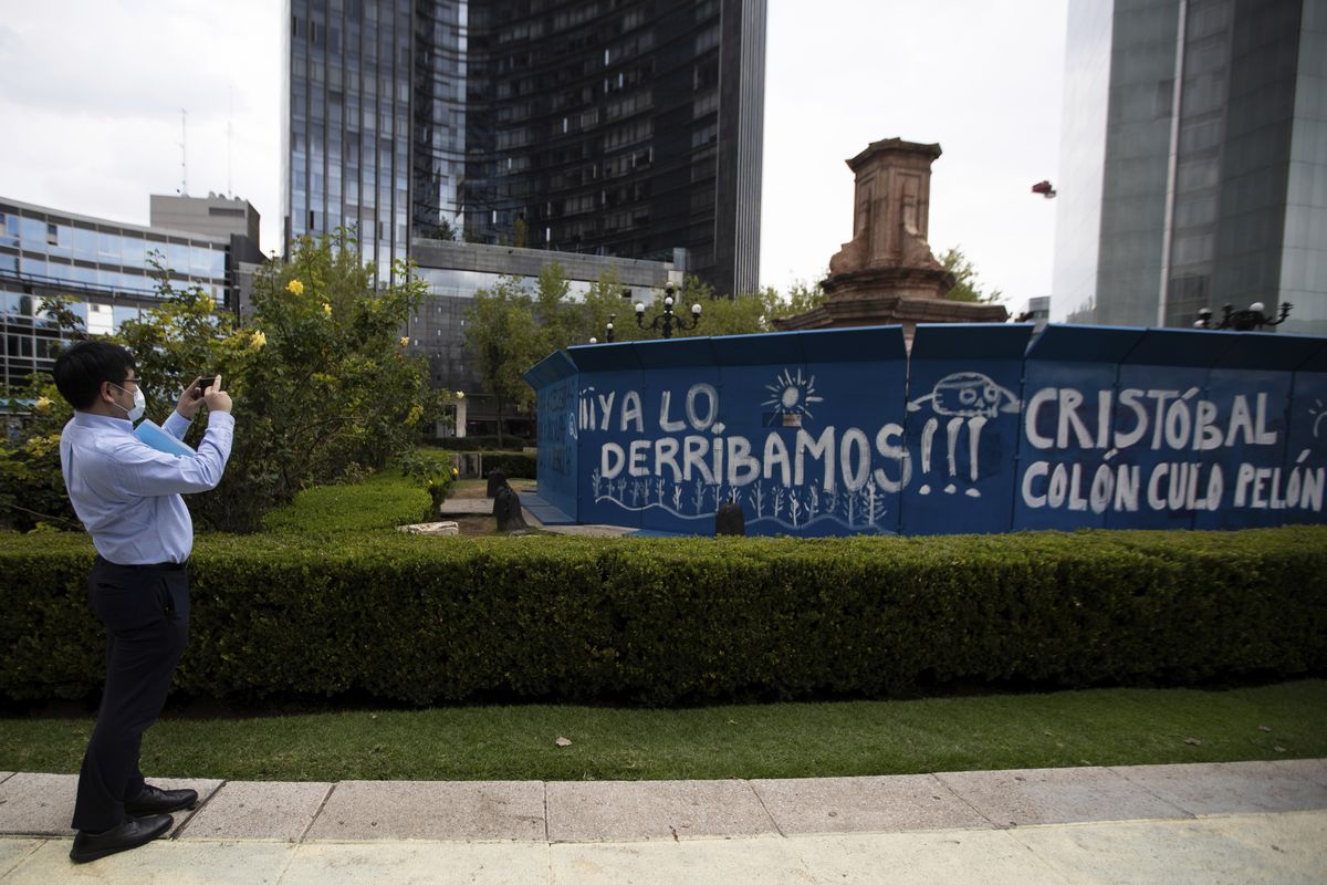 FILE - In this Oct. 12, 2020 file photo, a pedestrian takes a photo of graffiti on a temporary metal barrier set up to protect the perimeter of the Christopher Columbus