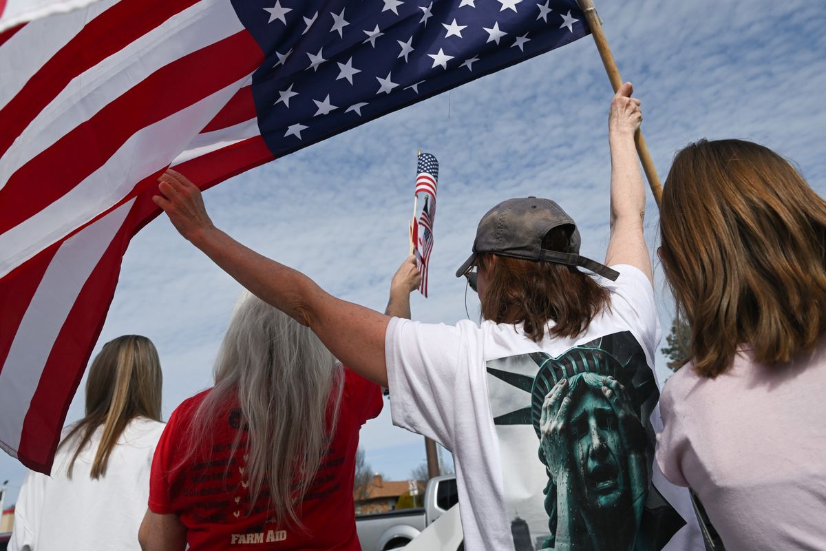 A woman who asked to remain anonymous waves an upside down American flag at passing motorists during a Hands Off! demonstration against the policies of President Donald Trump and Elon Musk on Saturday, Apr. 5, 2025, on Division Street in Spokane, Wash.  (Tyler Tjomsland/The Spokesman-Review)
