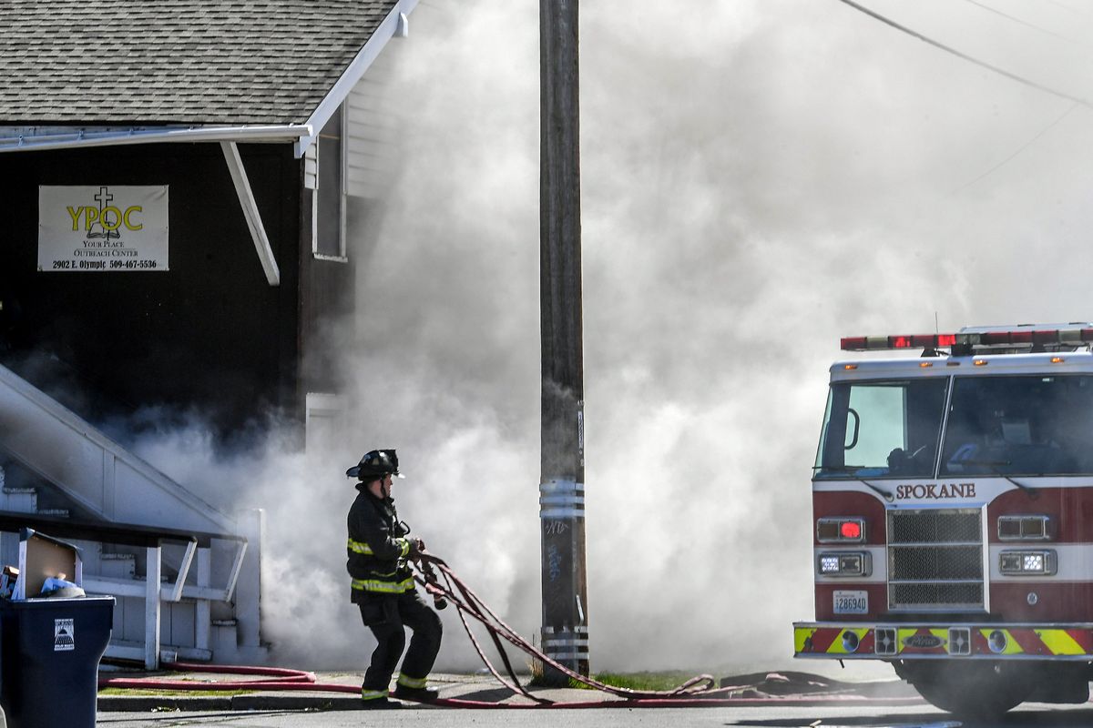 A firefighter pulls a hose as smoke billows from the front entrance area of the Your Place Outreach Center at the corner of Regal Street and Olympic Avenue, Tuesday, April 13, 2021, in Spokane.  (DAN PELLE/THE SPOKESMAN-REVIEW)