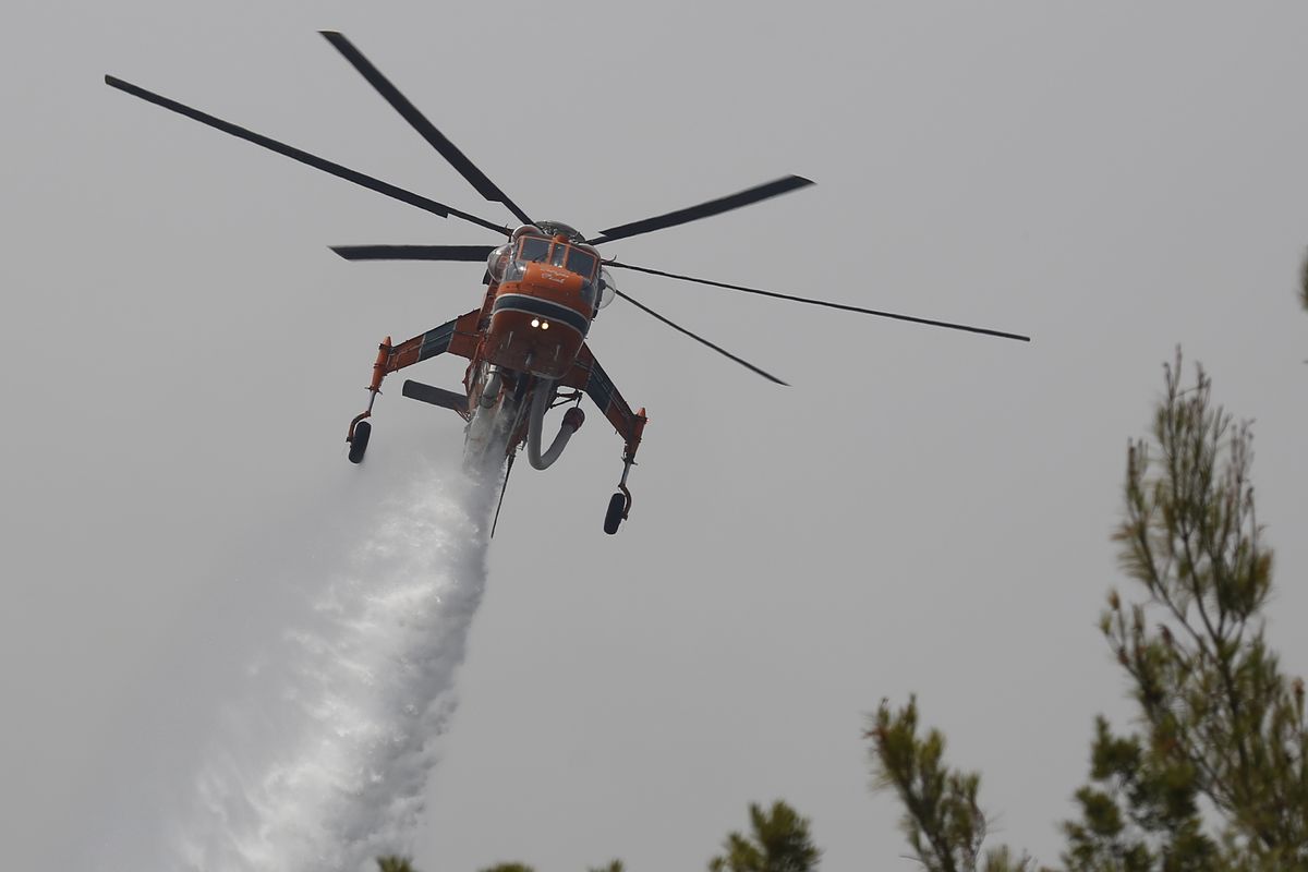 An helicopter drops water over a fire in Galatsonas village on Evia island, about 184 kilometers (115 miles) north of Athens, Greece, Wednesday, Aug. 11, 2021. Hundreds of firefighters from across Europe and the Middle East worked alongside Greek colleagues in rugged terrain Wednesday to contain flareups of the huge wildfires that ravaged Greece