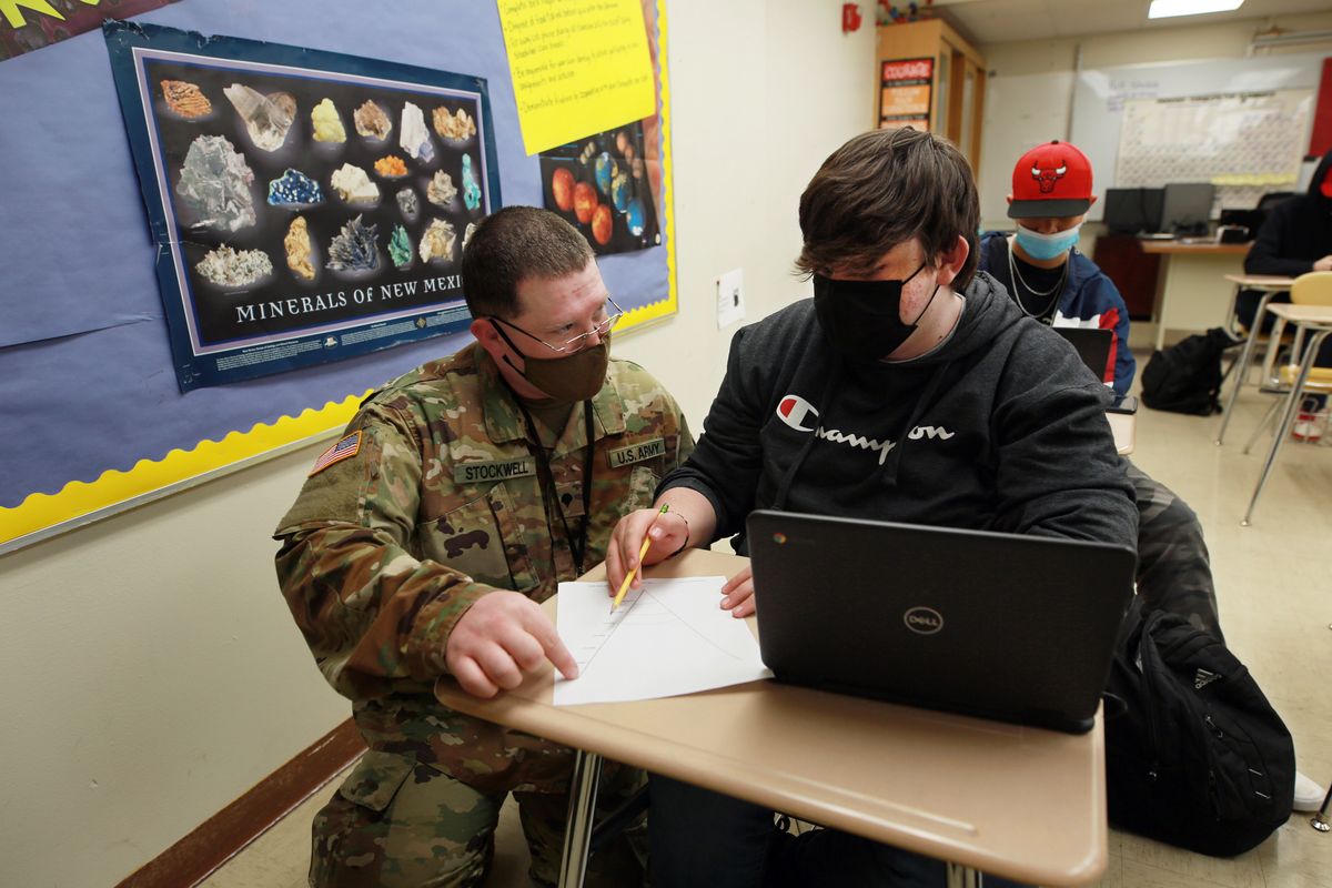 New Mexico Army National Guard specialist Michael Stockwell kneels while helping Alamogordo High School freshman Aiden Cruz with a geology assignment, at Alamogordo High School,Tuesday, Feb. 8, 2022, in Alamogordo, N.M. Dozens of National Guard Army and Air Force troops in New Mexico have been stepping in for an emergency unlike others they have responded to before: the shortage of teachers and school staff members that have tested the ability of schools nationwide to continue operating during the coronavirus pandemic.  (Cedar Attanasio)