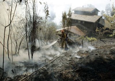 
A Los Angeles County firefighter pours water on foliage and trees that had been burning, sparing a home  in the Santa Monica Mountains as fire continues to burn in Malibu, Calif., Monday. Associated Press
 (Associated Press / The Spokesman-Review)