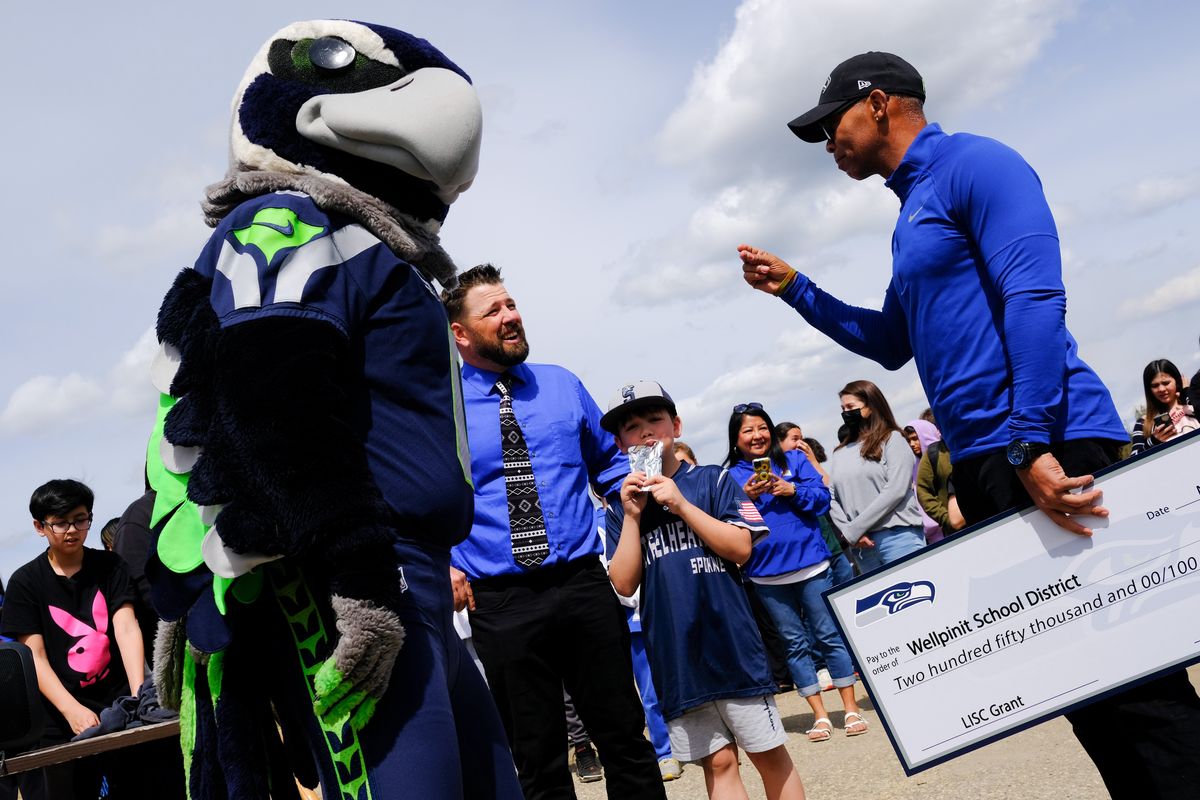 Clark Pauls, Wellpinit’s athletic director, center, chats with Paul Johns, right, the Seattle Seahawks’ director of youth and high school programs, while Seahawks mascot Blitz looks on during a groundbreaking ceremony for a new turf field Wednesday at Wellpinit High.  (Tyler Tjomsland/The Spokesman-Review)