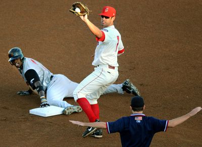 Salem-Keizer’s Vladimir Frias, left, and Spokane’s Matt West look to the bases umpire as he calls safe during Thursday night’s game. (Rajah Bose / The Spokesman-Review)