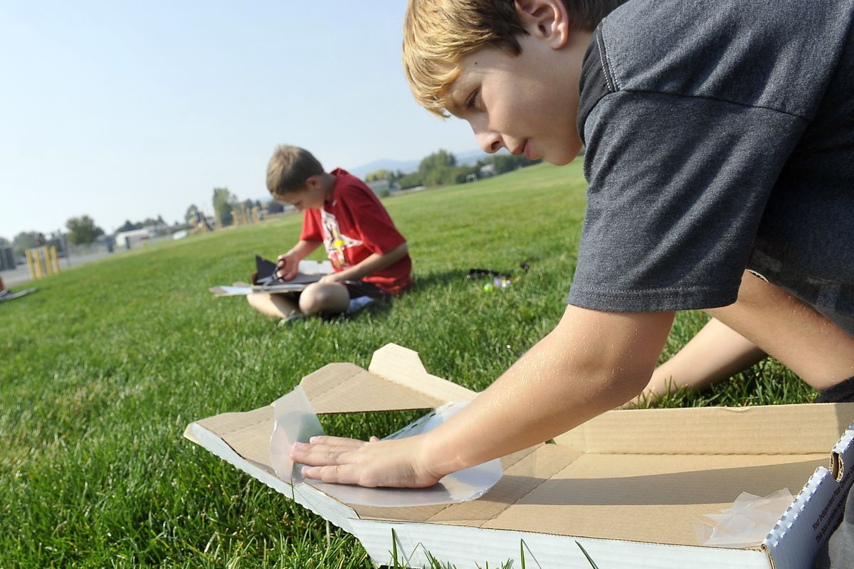 Fourth-grader Tyler Burghard, 10, right, tapes plastic into the lid of a pizza box to build a solar oven Wednesday at East Farms Elementary in Otis Orchards. The STEAM Magnet program gives students a chance to participate in a variety of projects and subjects, and the school is becoming a magnet school with the STEAM program as a theme. In the background is fellow student Hayden Ohl. (Jesse Tinsley)