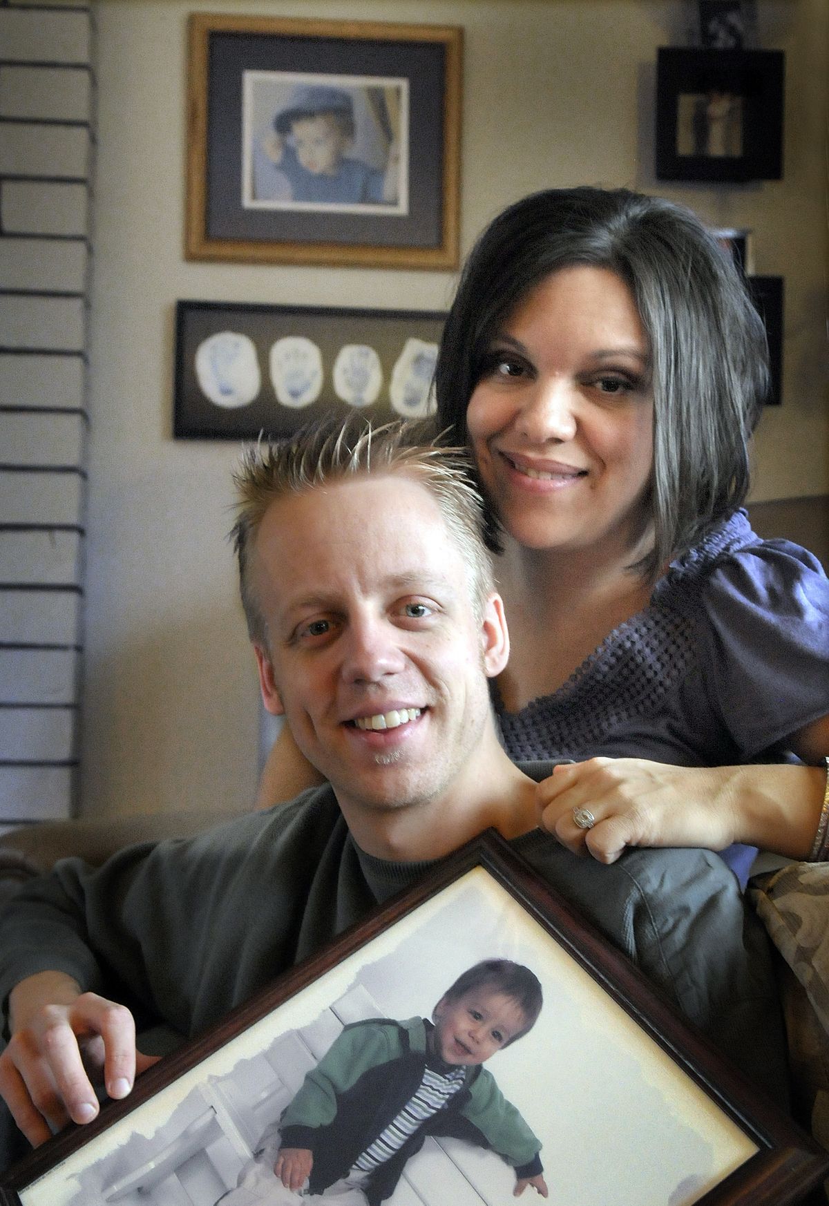 Eric and Jenna Miller are shown  with a photo of their son, Micah, who died  in  2003. The footprints and handprints of Micah are on the wall behind them.  (CHRISTOPHER ANDERSON / The Spokesman-Review)