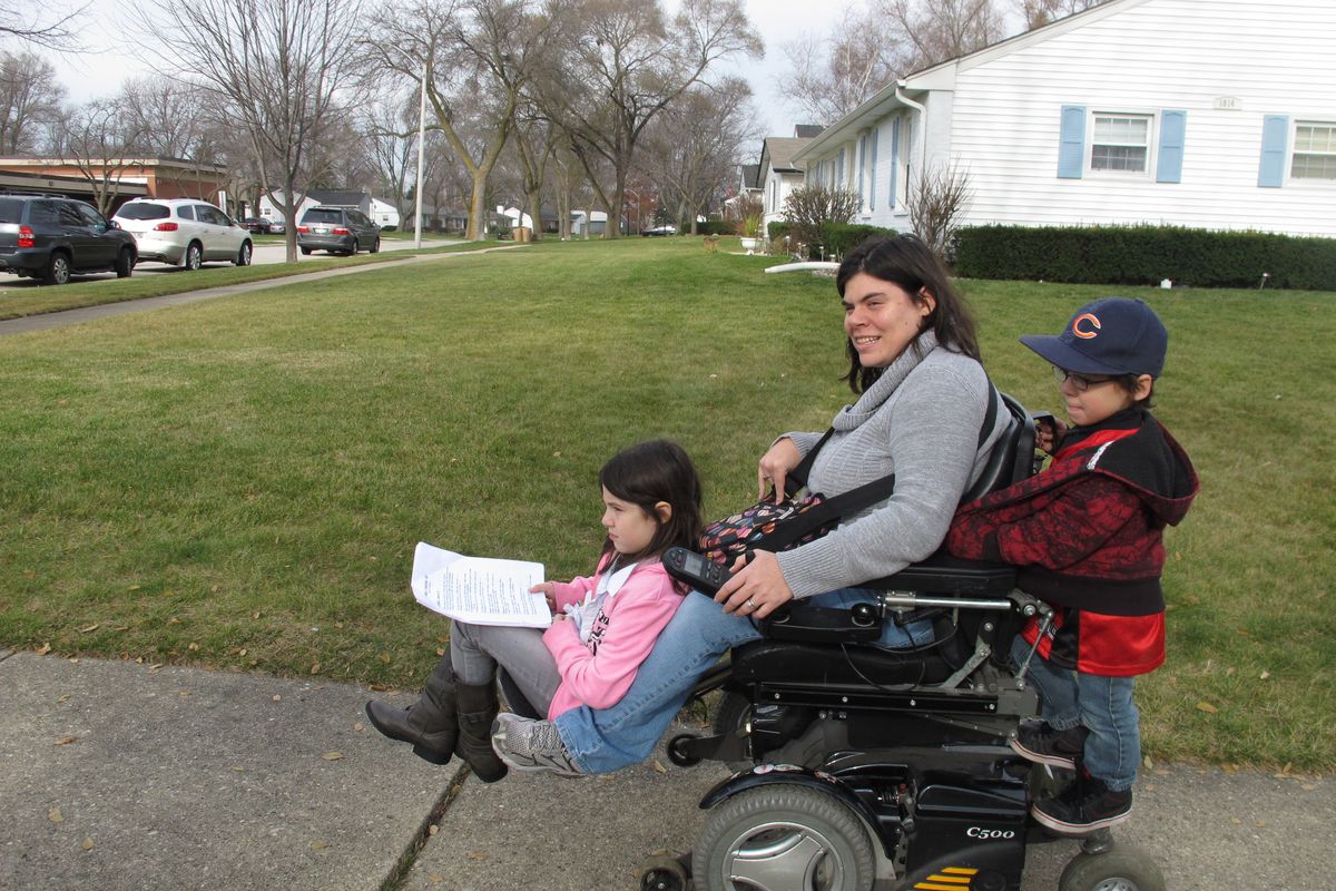 Twins Abigail and Noah Thomas, 8, ride on the motorized wheelchair of their mother, Jenn Thomas, on their way to a school book fair in Arlington Heights, Ill., on Nov. 19. Thomas, 36, has cerebral palsy. (Associated Press)