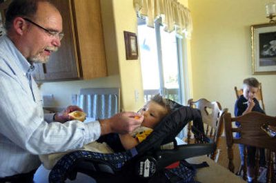 
Jerry Jackman feeds his 6-month-old grandson, Tauren Harris, while his other grandson, Shea Harris, 5, contemplates a drawing at Jackman's Spokane home. Jackman, a retired computer hardware supervisor, takes care of his grandchildren while his wife, daughter and son-in-law work full time. 
 (Photos by HOLLY PICKETT / The Spokesman-Review)