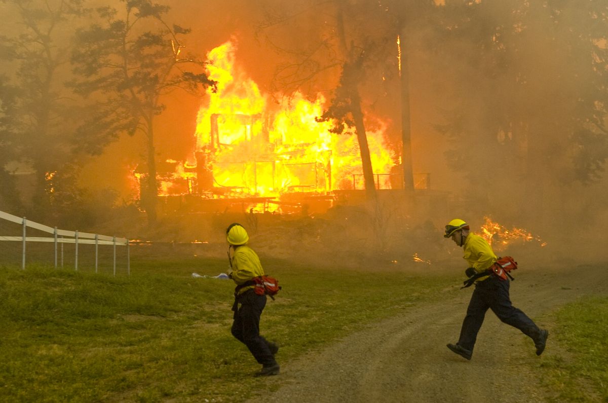 Spokane County firefighters run past owner Jim Gibbard’s burning house at 9700 E. 24th Ave., July 11, 2008. The wildfire destroyed eight homes.  (File photo / The Spokesman-Review)