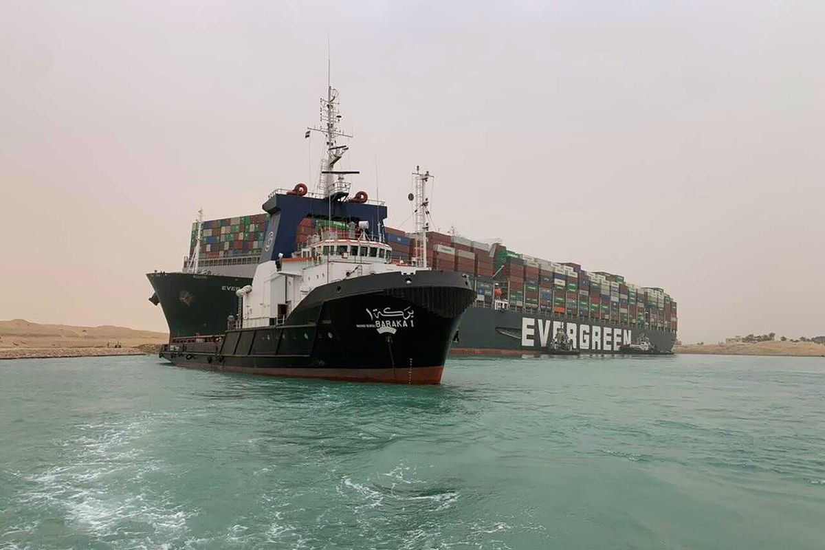 CORRECTS NAME OF SHIP TO EVER GIVEN, NOT EVER GREEN - In this photo released by the Suez Canal Authority, a boat navigates in front of a cargo ship, Ever Given, Wednesday, March 24, 2021, after it become wedged across Egypt’s Suez Canal and blocked all traffic in the vital waterway. An Egyptian official warned Wednesday it could take at least two days to clear the ship.  (HOGP)