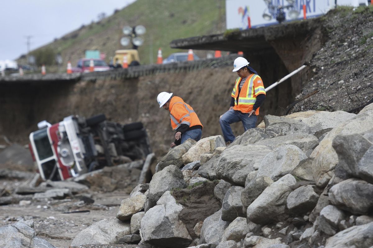 In this Feb. 18 photo, crews look over a tractor-trailer and a San Bernardino County Fire Department fire engine that fell from southbound Interstate 15 where part of the freeway collapsed due to heavy rain in the Cajon Pass in California. A state $5 billion annual plan raises fuel taxes and vehicle fees to pay for repairs to state and local roads, while also providing money for public transit and biking and walking trails. (David Pardo / Associated Press)