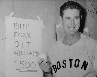 Ted Williams, Boston Red Sox aging slugger, displays the baseball he hit in June 18, 1960 game, for the 500th home run of his major league career. The homer beat Cleveland 3-1. An usher retrieved the ball and gave it to Williams for a souvenir. Taped on the dressing room wall is the list of the only major league players ever to reach the 500 home run figure – Babe Ruth, Jimmy Foxx, Mel Ott, and Williams.  (Associated Press)