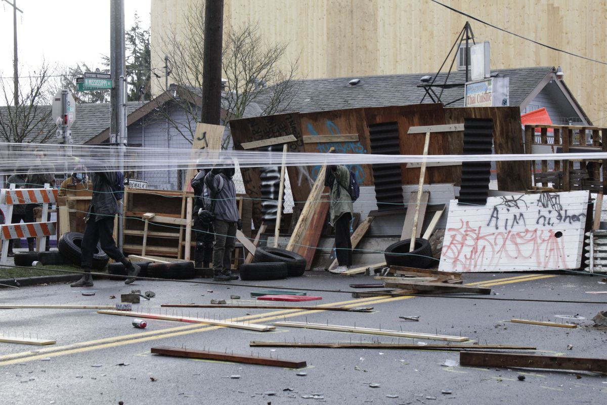 Protesters stand behind barricades at their encampment outside a home in Portland, Ore., on Wednesday, Dec. 9, 2020. Makeshift barricades erected by protesters are still up in Oregon