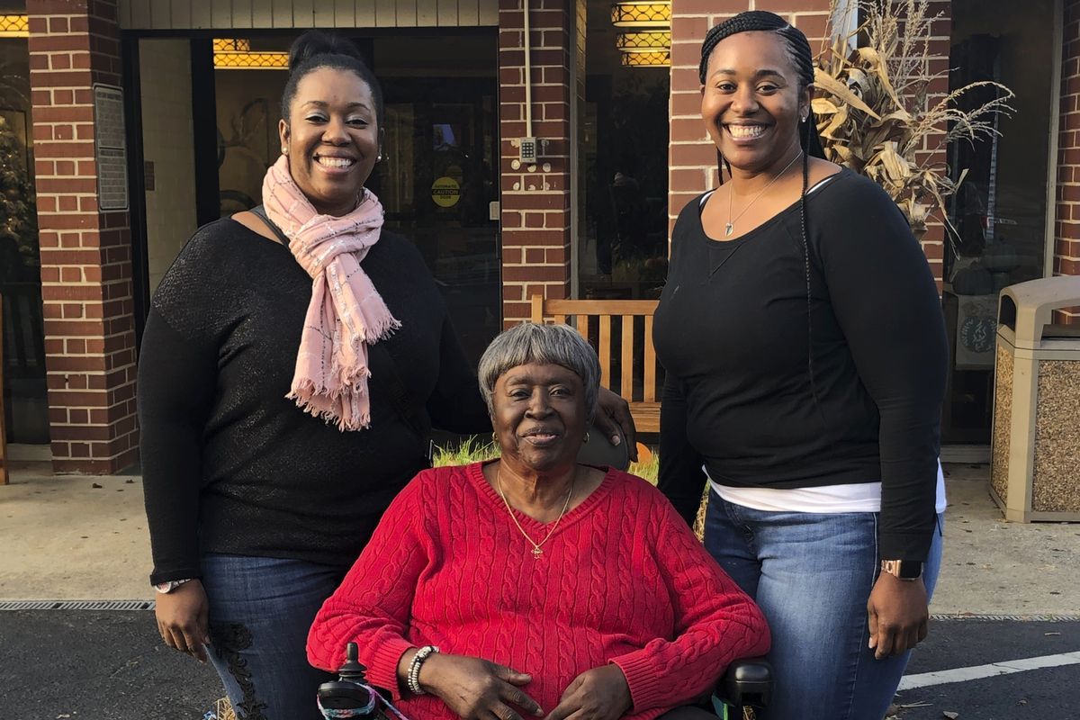In this Nov. 28, 2019, photo provided by the Burrough family, Bessie Burden, center, poses with her daughters Theresa Burrough, left, and Lashieka Mitchell outside the Westbury Conyers nursing home in Conyers, Ga. Burden died Oct. 22, 2020, after becoming infected with the coronavirus during an outbreak at the nursing home. Burden’s daughters blame the home for their mother’s death, saying administrators kept the family in the dark about Burden being exposed to the virus and quarantined as a presumptive case. But the state has essentially blocked them from going to court.  (Leah Burrough)