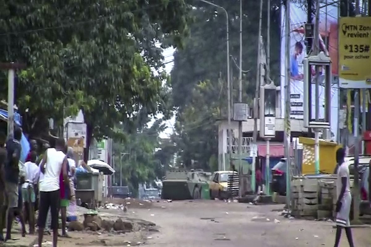 In this image made from video, residents watch as an armored personnel carrier is seen on the streets near the presidential palace in the capital Conakry, Guinea Sunday, Sept. 5, 2021. Mutinous soldiers detained President Alpha Conde on Sunday after hours of heavy gunfire rang out near the presidential palace, then announced on state television that the government had been dissolved in an apparent coup d