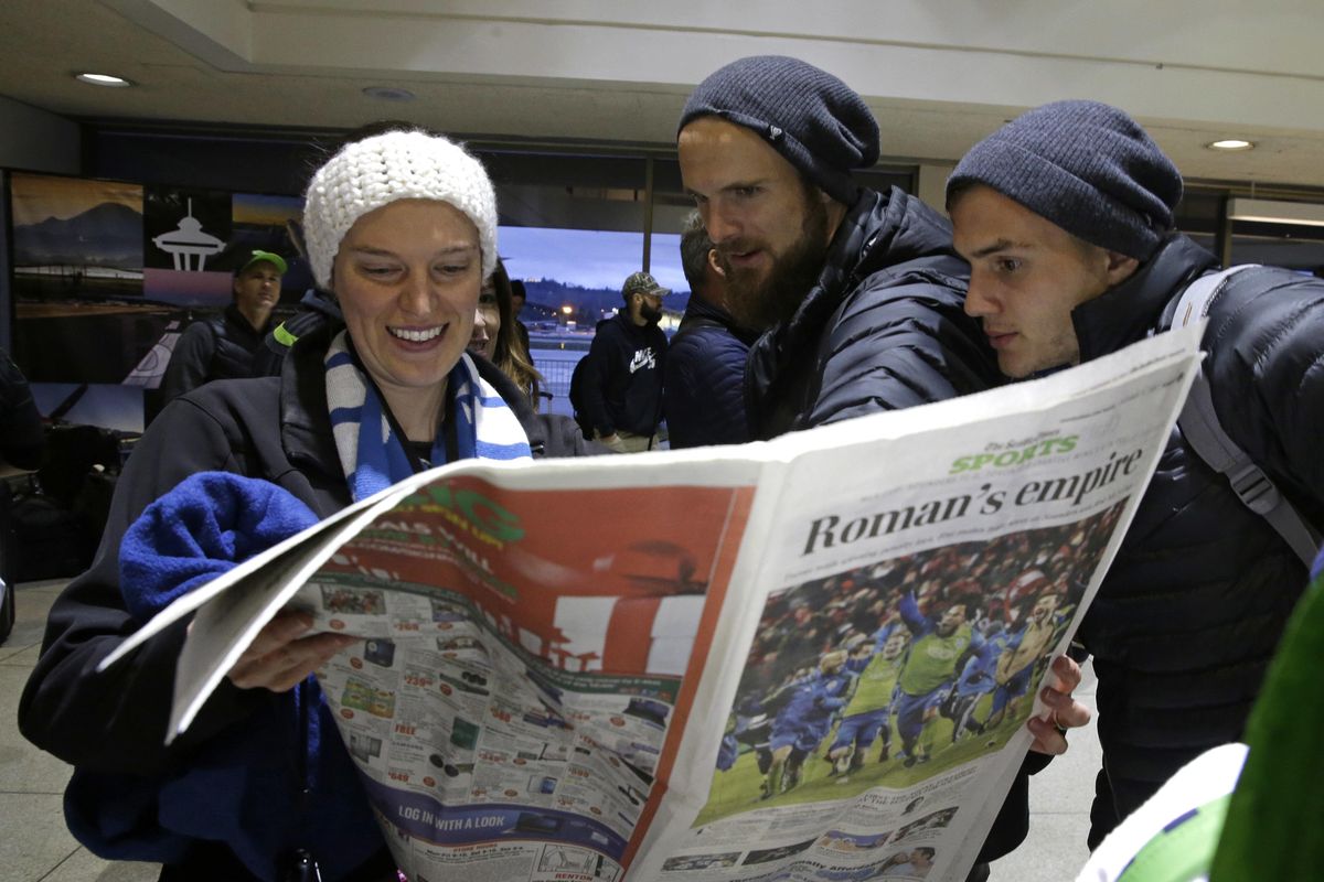 Seattle Sounders forward Jordan Morris, right, and goalkeeper Stefan Frei, second from right, check out the Sunday edition of the Seattle Times on Sunday, Dec. 11, 2016, at the King County Airport. (Ted S. Warren / Associated Press)