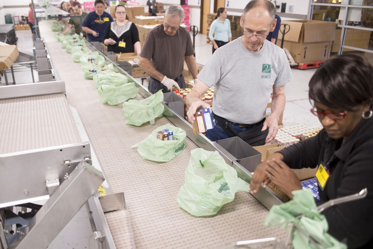 Volunteers, from right, Kathy Jones-Taylor, Albert Rose and John Erickson pack Bite2Go bags on an assembly line at Second Harvest Friday, Aug. 25, 2017. The kits, given to children suspected of having insufficient or unpredictable access to food at home, contains healthy snack foods. (Jesse Tinsley / The Spokesman-Review)