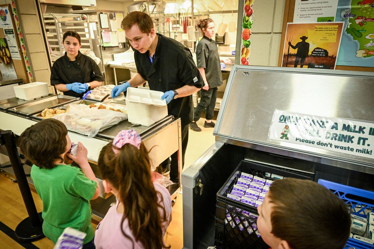 WSU graduate students Evan Trujillo, above, and Sara Evers, upper left, serve lunch to kindergarten and first-grade students at Sunset Elementary as they line up and choose milk, either nonfat or 1%, to drink from the cooler at right at their school in Airway Heights. Trujillo and Evers are working on a degree in nutrition and exercise physiology. Federal school lunch guidelines were recently changed to allow whole milk as a drink option in schools.  (Jesse Tinsley/The Spokesman-Review)