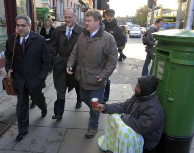 Ajai Chopra, left, deputy director of the European Department of the IMF,  passes a beggar on his way to the Central Bank of Ireland  in Dublin on Thursday.  (Associated Press)