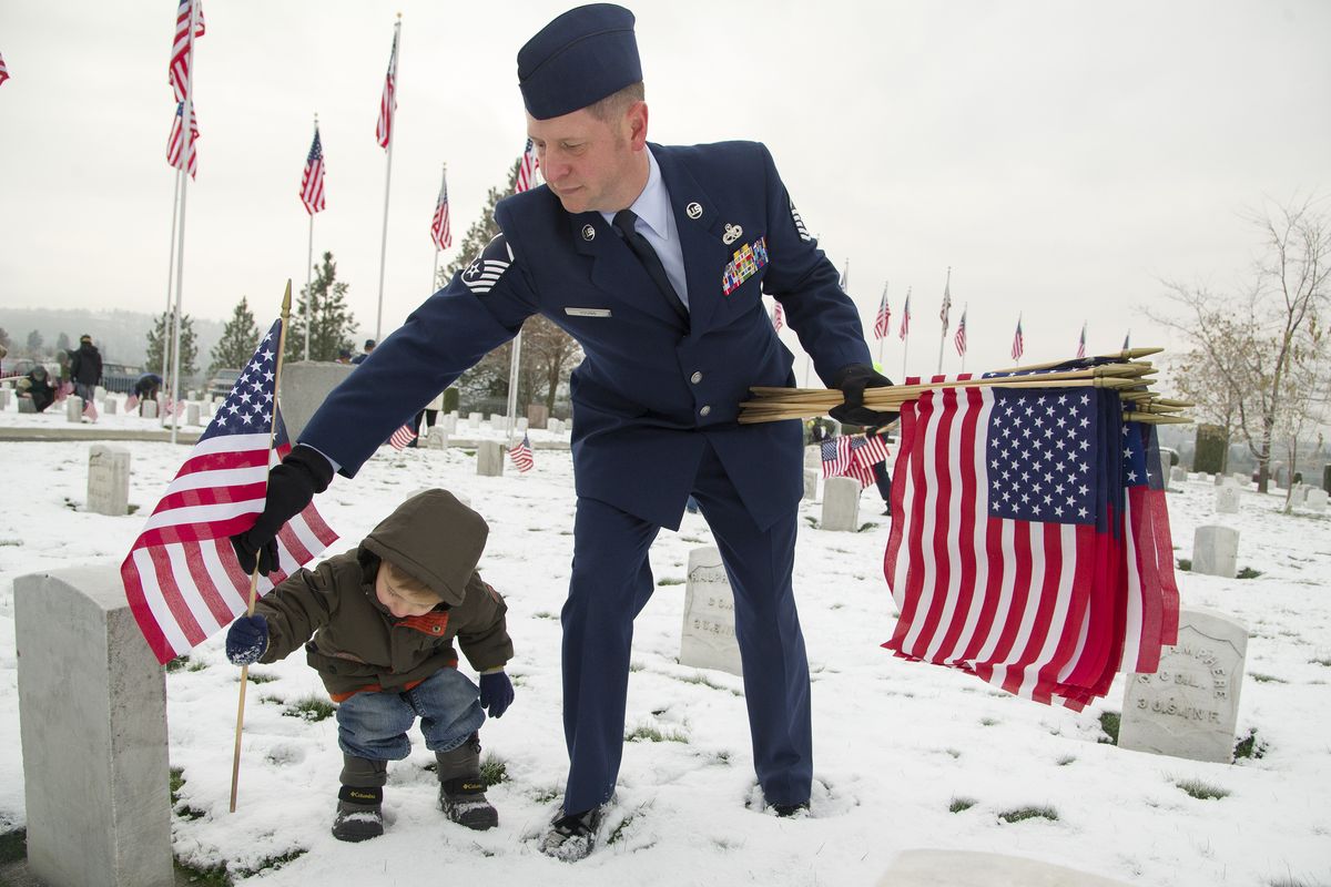 Master Sgt. Jason Young from Fairchild Air Force Base and his son Cooper, 3, place American flags next to gravestones of U.S. military veterans before the Veterans Day ceremony Sunday at Fort George Wright Cemetery. (Colin Mulvany)