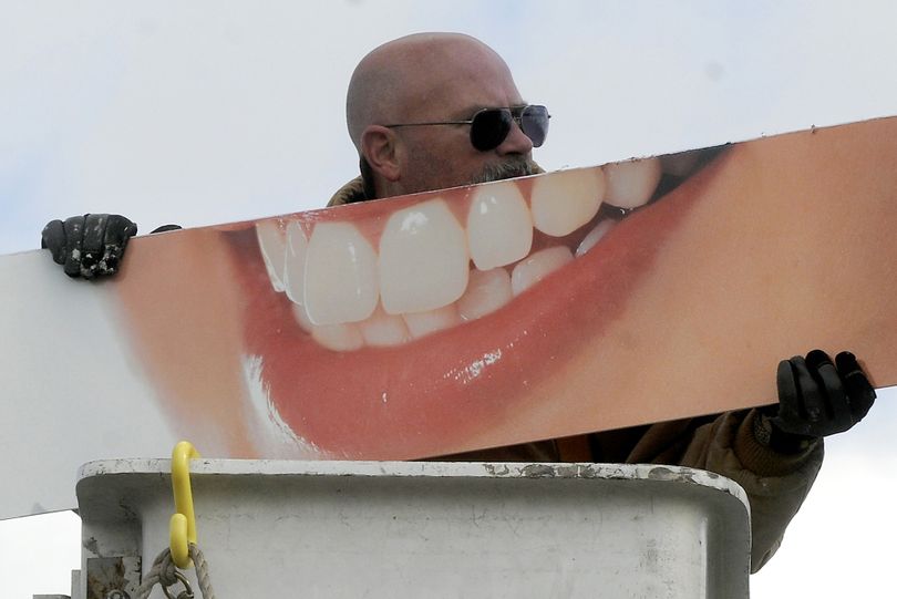 Steve McQuistion, an employee of Sign Affects, looks like he's showing off his oversized pearly whites Thursday, Nov. 10, 2011 as he hangs a dentist sign at the Tower Building in Springfield, Ohio. (Marshall Gorby / Springfield News-sun)