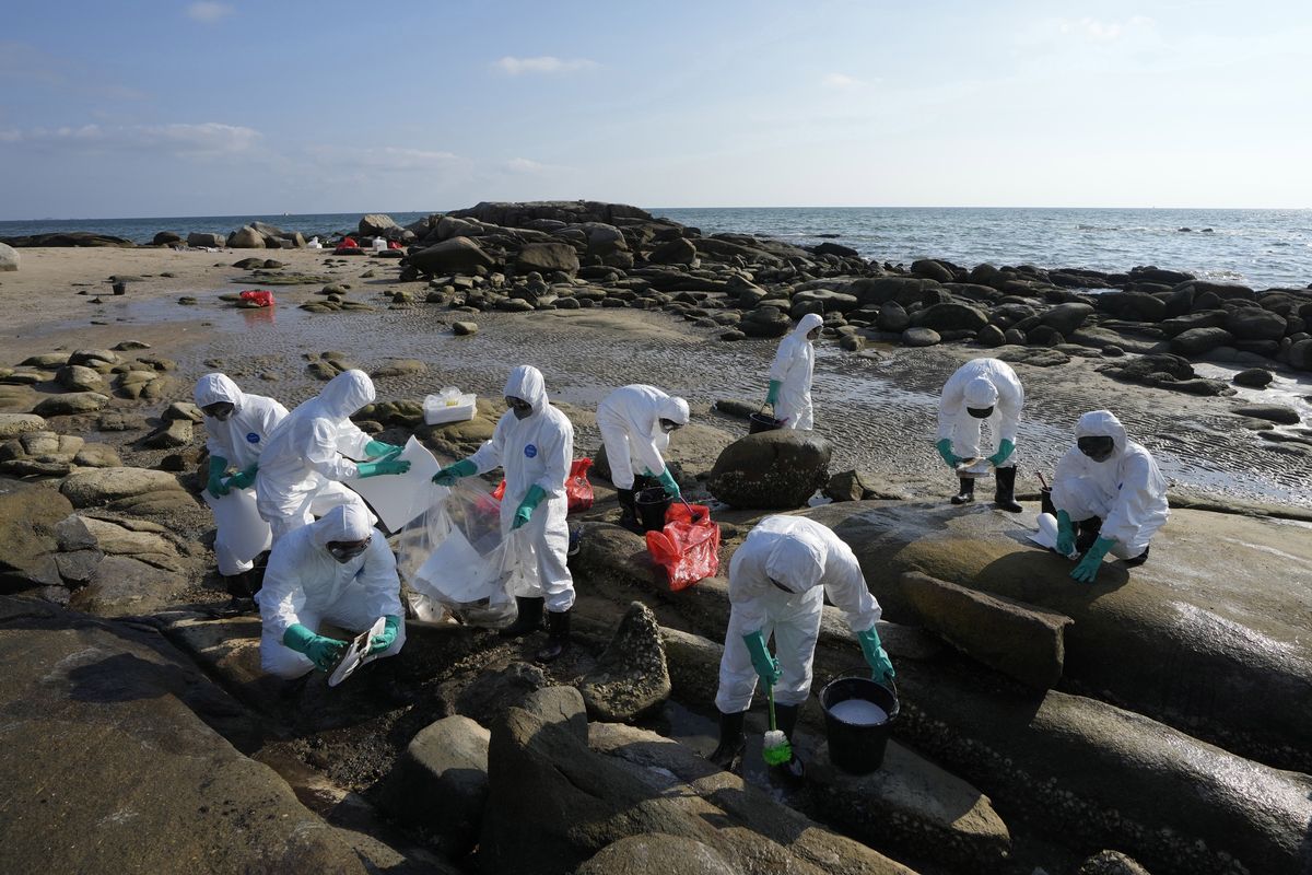 Workers scrubbing oil off rocks on Mae Ramphueng Beach after a pipeline oil spill off the coast of Rayong province in eastern Thailand, Sunday, Jan. 30, 2022. The governor of a province in eastern Thailand on Saturday declared a state of emergency after an oil slick washed up on a sand beach, shutting down restaurants and shops in a setback for the pandemic-hit tourism industry.  (Sakchai Lalit)
