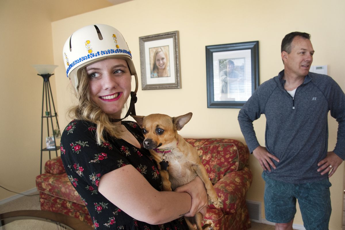 McKenzie Capka had a stroke at age 18 in her dorm room at the University of Montana last winter. While she was in the ICU, a family friend started a GoFundMe campaign for her that has raised more than $30,000. Capka, who wears a helmet to protect an open part of her skull after brain surgery, holds her new dog Ginger at their Spokane home on May 29. Her father, Mike, is in the background. (Dan Pelle)