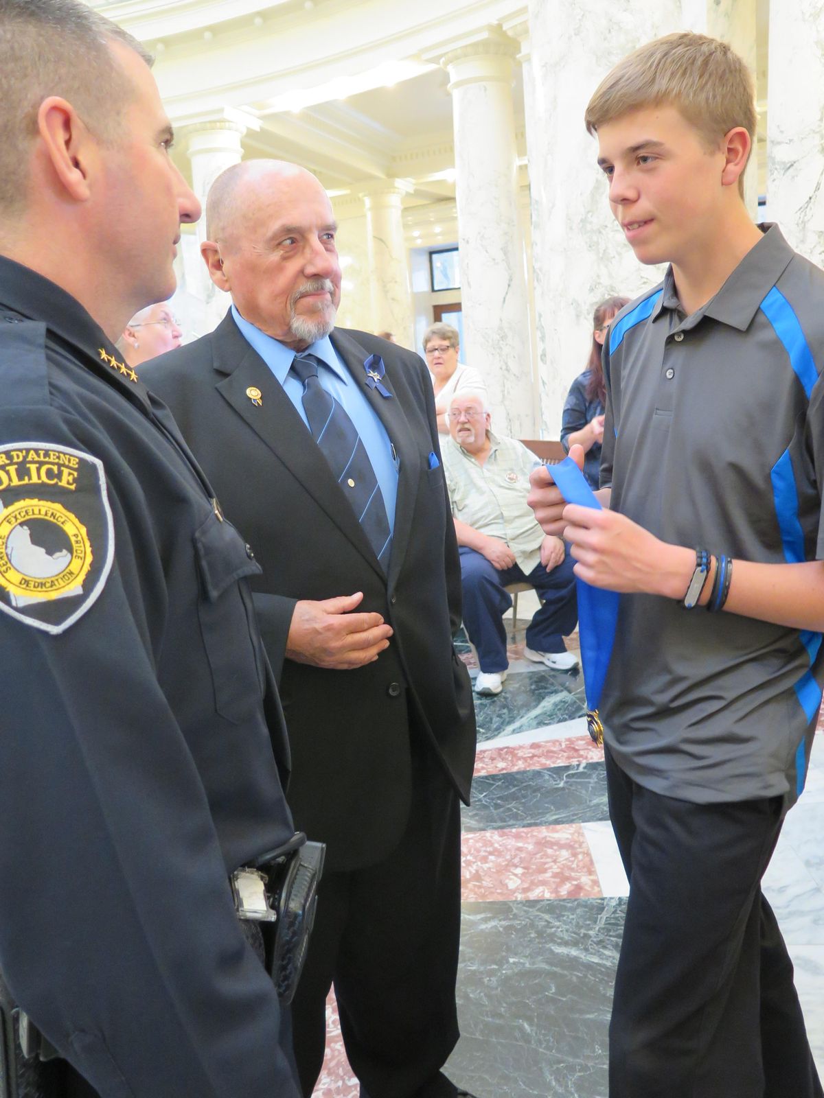 Dylon Moore, 14, right, holds the Idaho Medal of Honor he received Wednesday at the state Capitol for his late father, Coeur d’Alene Police Sgt. Greg Moore, and talks with Coeur d’Alene Police Chief Lee White, left; at center is Fred Moore, Greg Moore’s father. (Betsy Z. Russell / Betsy Z. Russell/The Spokesman-Review)